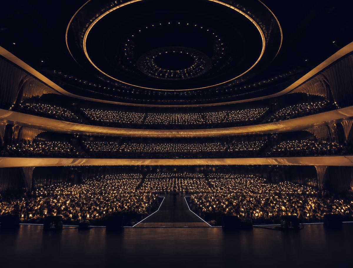 An auditorium of fans holding warm golden lights, seen from the stage.
